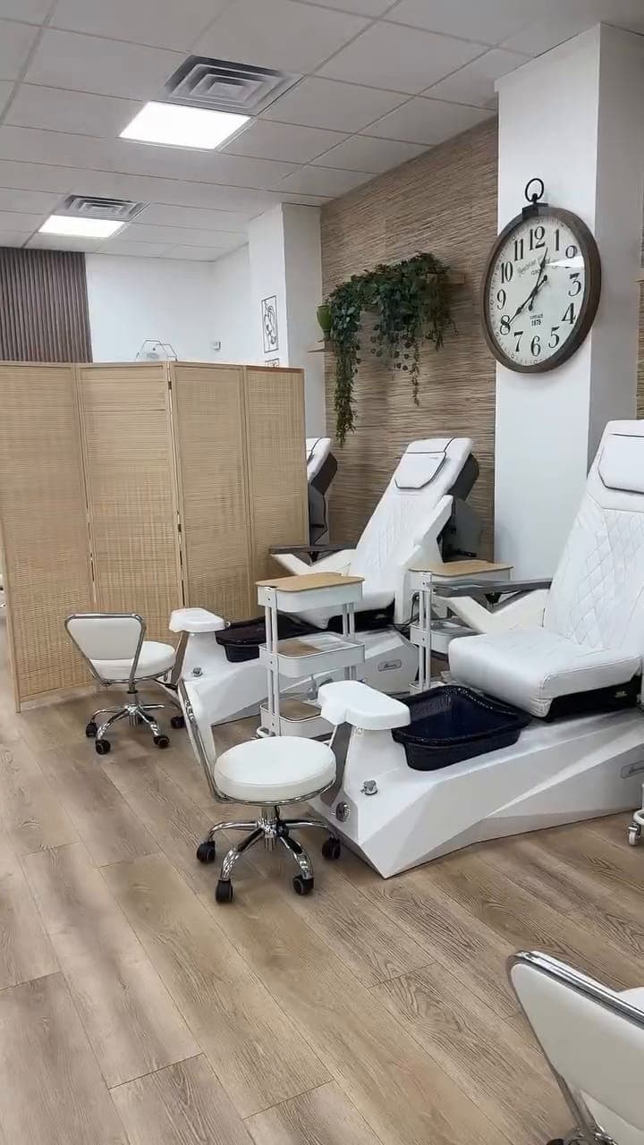 White pedicure chairs along a grasscloth wall with greenery and a clock